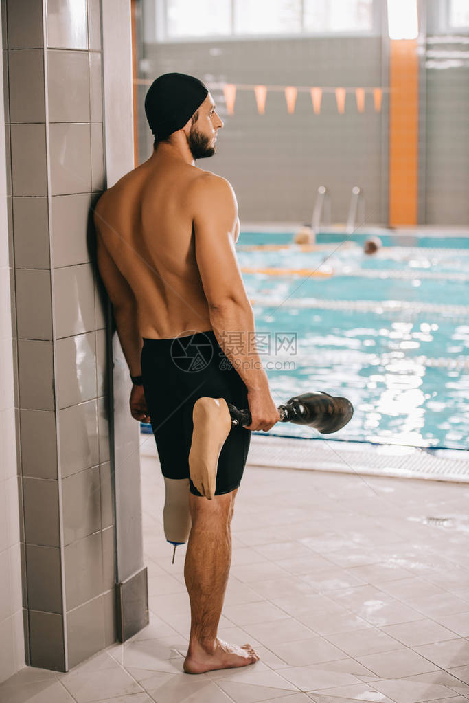 站在室内游泳池的泳池边握着他的人工腿图片