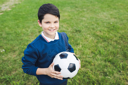 快乐的孩子拿着足球看着草地的背景图片