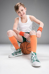 穿着运动服的笑着男孩坐在篮球上孤图片