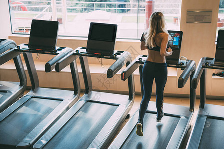 妇女在健身房的跑步机上运行窗式运动机图片