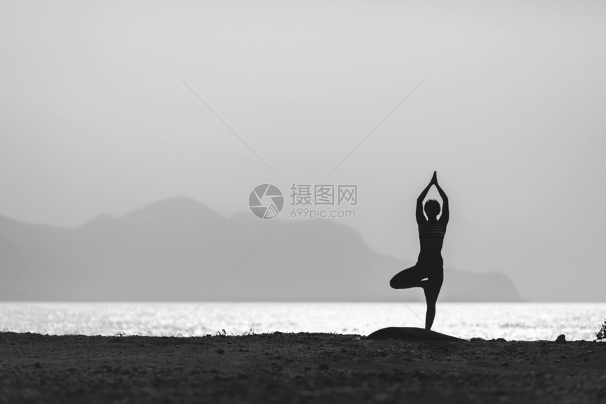 在瑜伽Vrksasana中冥想的女人在海洋海滩和山脉中构成剪影动机和鼓舞人心的锻炼户外自然的健康生活方图片