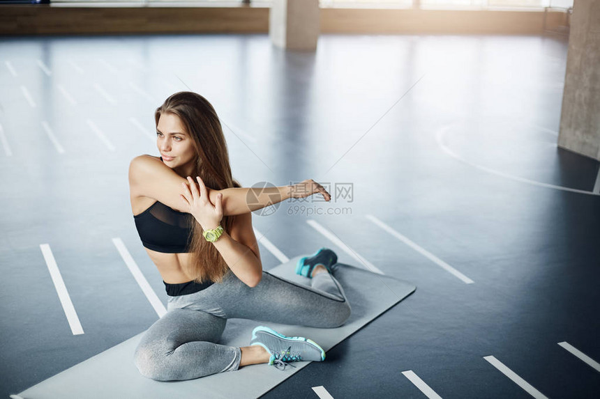 年轻金发碧眼的成年女子在健身房伸展手臂为她的图片