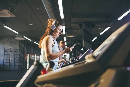 主题运动和音乐一个美丽的白种女人在跑步机上的健身房里跑步戴着大白耳机图片