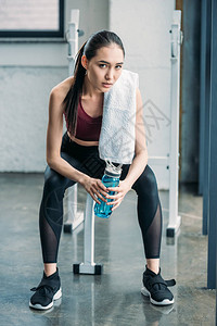 体操锻炼后用运动水瓶和毛巾休息的年青图片
