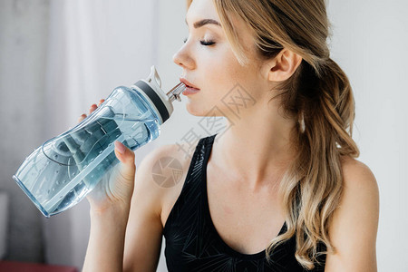 灰色背景下运动女从运动水瓶中图片