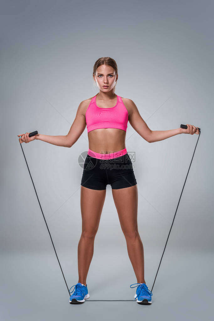 一个漂亮的健身女人在灰色背景下用跳绳锻炼的全长图像与美丽苗条健康的身体摆在工作图片