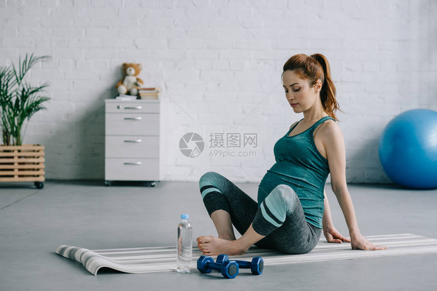 美丽的孕妇在瑜伽垫上伸腿的侧面图片