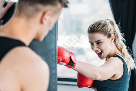 男教练在健身房里用沙袋看攻击女运动员拳击图片