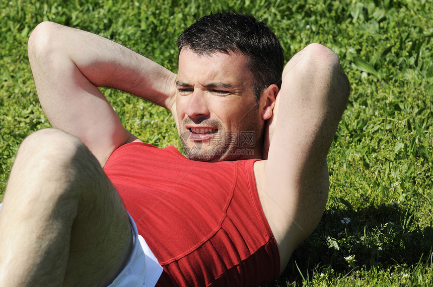 有魅力的男人正在新鲜的草地上做仰卧起坐图片