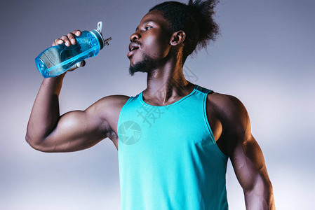 以灰色和蓝色梯度为背景照明用运动瓶饮酒的年轻肌肉强壮的非洲图片