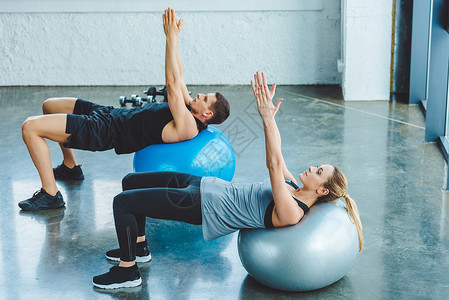 年轻男女在健身房的健身球上锻炼图片
