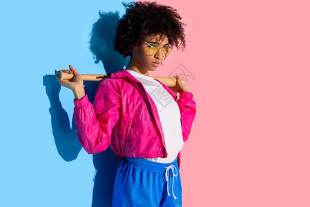带着棒球棍的年轻非洲女孩她肩膀上穿着粉红和蓝色背图片