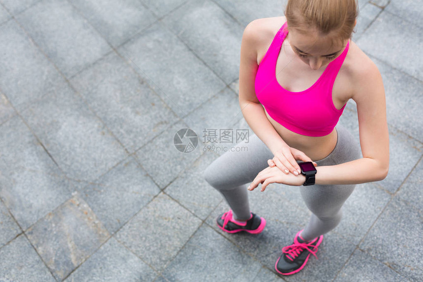 看智能手表的女跑步者运动员使用她的健身追踪器查看有氧运动期间的进展或心率在城市户外训练的女孩技术和积极的图片