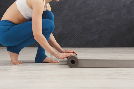 普拉提背景训练后卷起瑜伽垫的无法辨认的女人练习瑜伽之前或之后的体育课图片