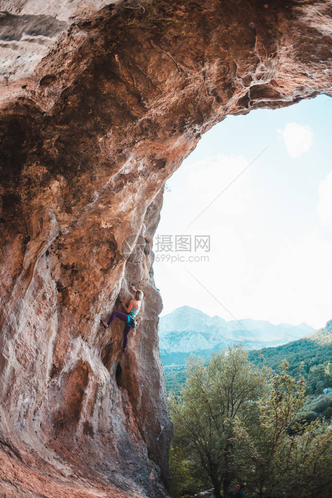 一个女人爬上岩石以拱形的式岩石洞穴极限运动运动员在自然浮雕上训练运动员克服了艰难的攀登路线图片