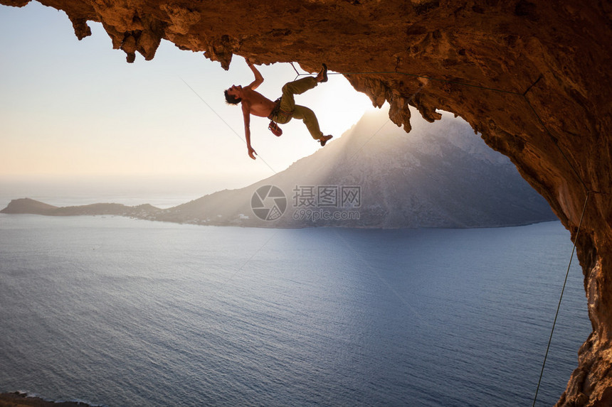 攀岩者在日落时沿着洞穴的屋顶攀爬图片