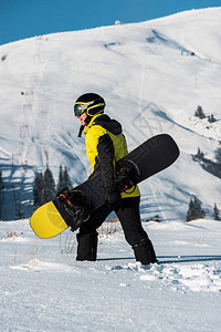 戴着头盔的滑雪者带着滑雪板在山上行走的侧视图图片