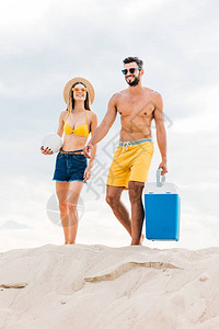 身着沙滩服装排球和便携式冰箱的年轻美女夫妇图片