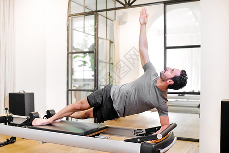 健康和健身概念的健身男子在健身房的改革床上做普拉图片