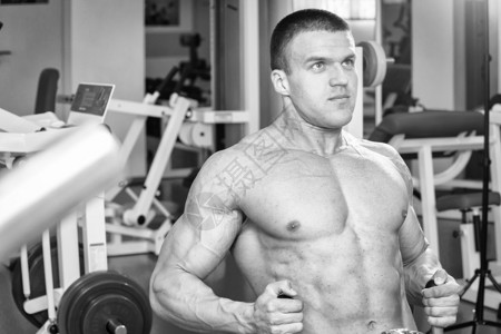 健身房里的肌肉男锻炼手臂肌肉在模拟器上训练在他的身图片
