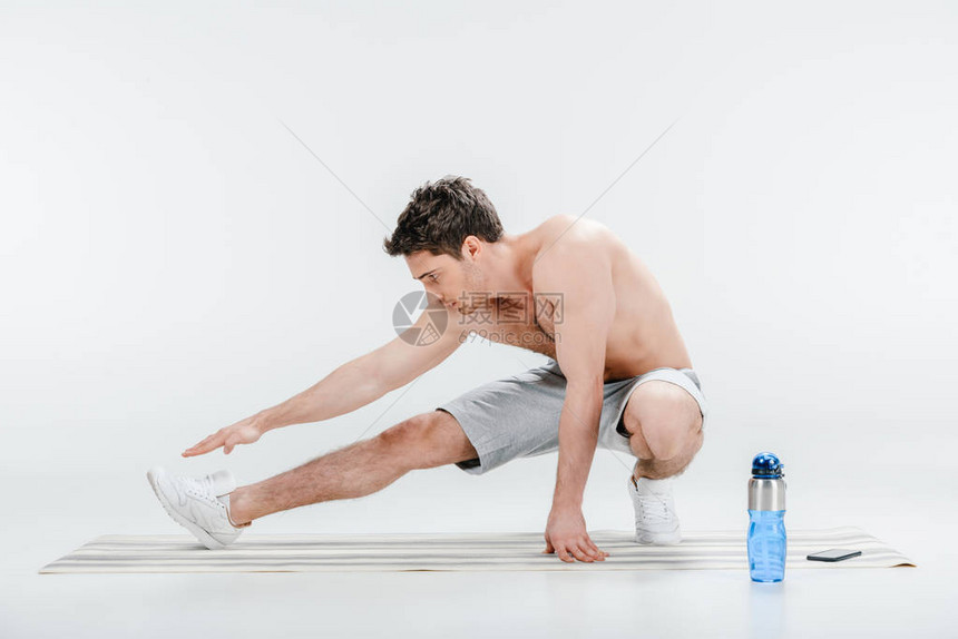 英俊的年轻人在瑜伽垫上伸展与白色隔离图片