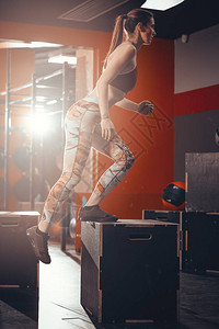 年轻健康的女人在健身房跳上箱子背景图片