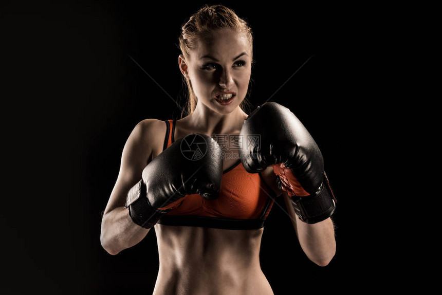 在黑色隔离的拳击手套中攻击年轻女运动员拳图片