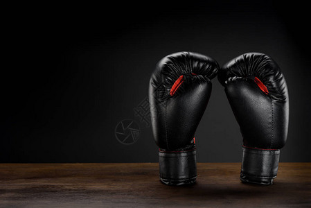 黑色拳击手套放在深色木质表面上的特写镜头背景图片