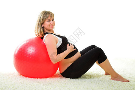 孕妇在白色背景上用红色体操球锻图片