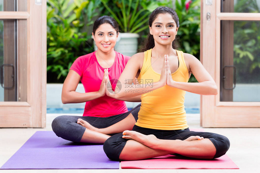 在室内练习瑜伽期间两名年轻妇女坐在图片
