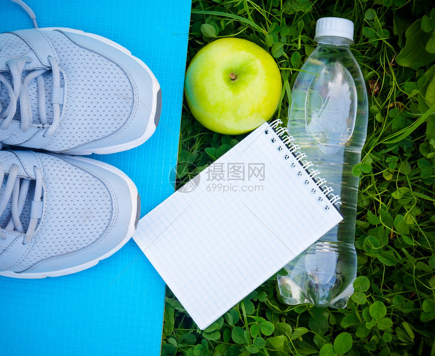 瑜伽垫水瓶和新鲜绿草上的苹果上运动鞋运动鞋在开放图片