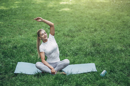 健身女人在清晨公园准备瑜伽穿着时尚的运动装蓝色瓶装水和瑜伽垫健图片