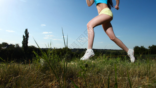 年轻运动女腿穿过青绿草与蓝图片