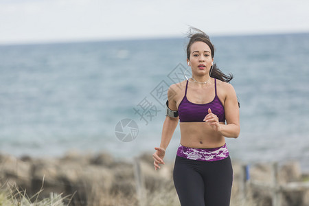 身穿健身服的年轻运动女运动员在寒冬多云的海滩边图片