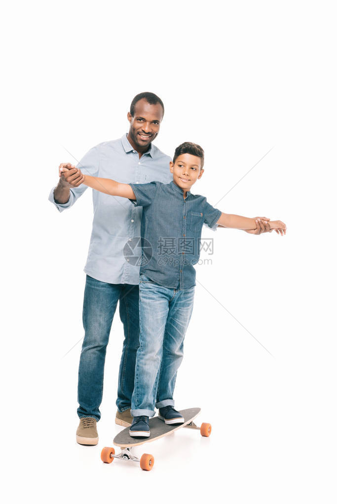 快乐的非洲裔美国父亲牵着微笑的儿子的手站在滑板上图片