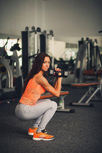体育年轻女孩在健身房用哑铃蹲下健身运动训练健身房和图片