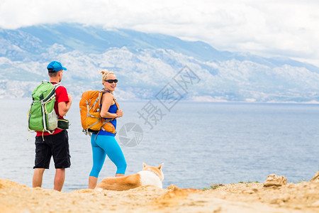 幸福的情侣徒步旅行者带着秋田犬在夏季山区徒步旅行图片