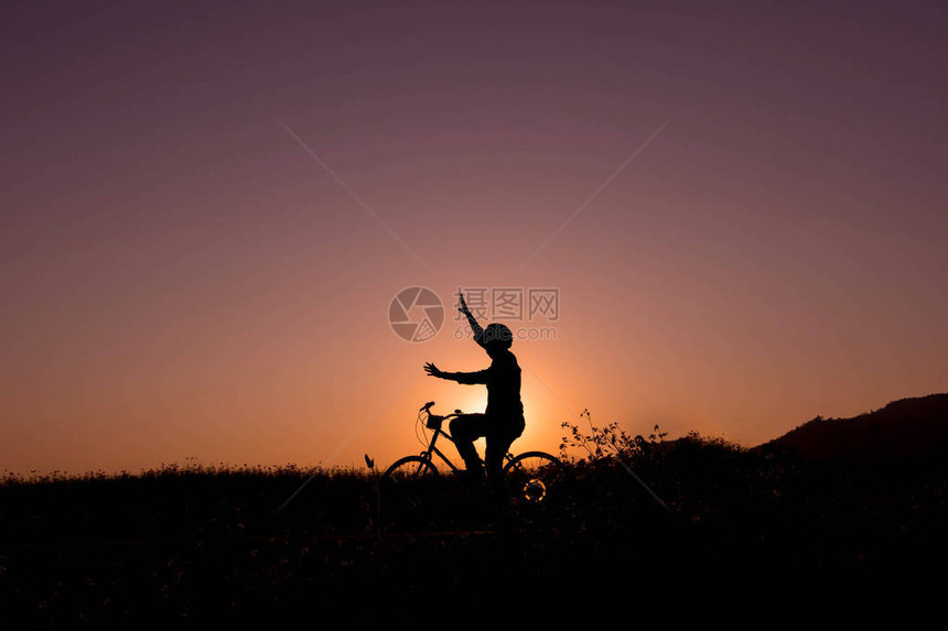 在自然日出或日落时用举起的手臂骑着自行车带双臂的快乐人的休眠图片