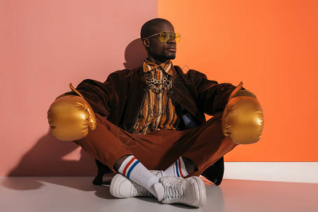 有自信的非洲时尚男子身着金拳手套坐在工作室看风景图片