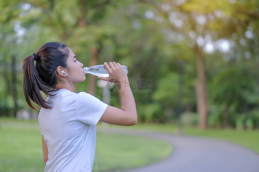年轻健身女在户外公园散步时喝能量水图片