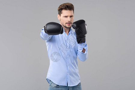 灰色工作室背景上穿着蓝色牛仔裤和蓝色衬衫戴着黑色拳击手套的图片