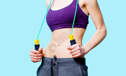 女人在蓝色背景下减肥后用跳绳展示她的腹肌图片