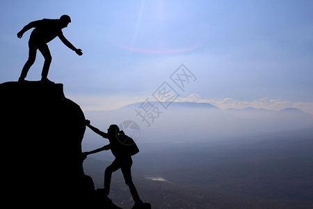 团队的朋友徒步旅行帮助彼此信任中的援助剪影徒步者在登山队顶上互相帮图片