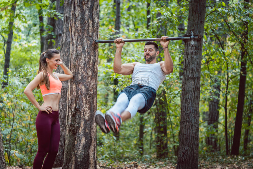 女人看着男人在森林健身房的高级图片