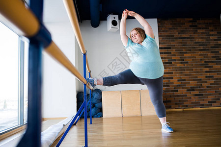 在芭蕾舞课上用窗边伸腿的优雅肥胖女图片