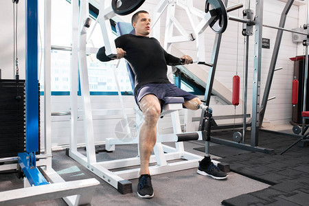 在现代健身房使用机器推举重物锻炼假腿的英俊肌图片