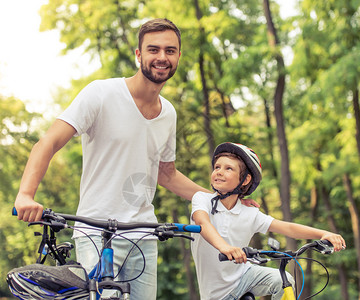 英俊的年轻爸和他可爱的小儿子在公园里骑自行车父亲在看相机图片