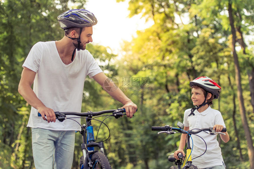 英俊的年轻爸和他可爱的小儿子在公园骑自行车的时候互相看着图片