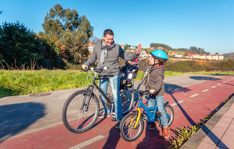 快乐的父亲和儿子通过成功学习在阳光明媚的冬季日子里在城市骑自行车图片
