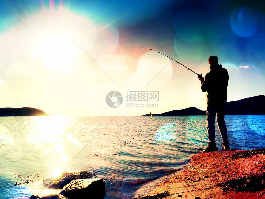 镜头缺陷活跃的人从岩石海岸在海上钓鱼渔夫检查钓鱼线上的诱饵图片